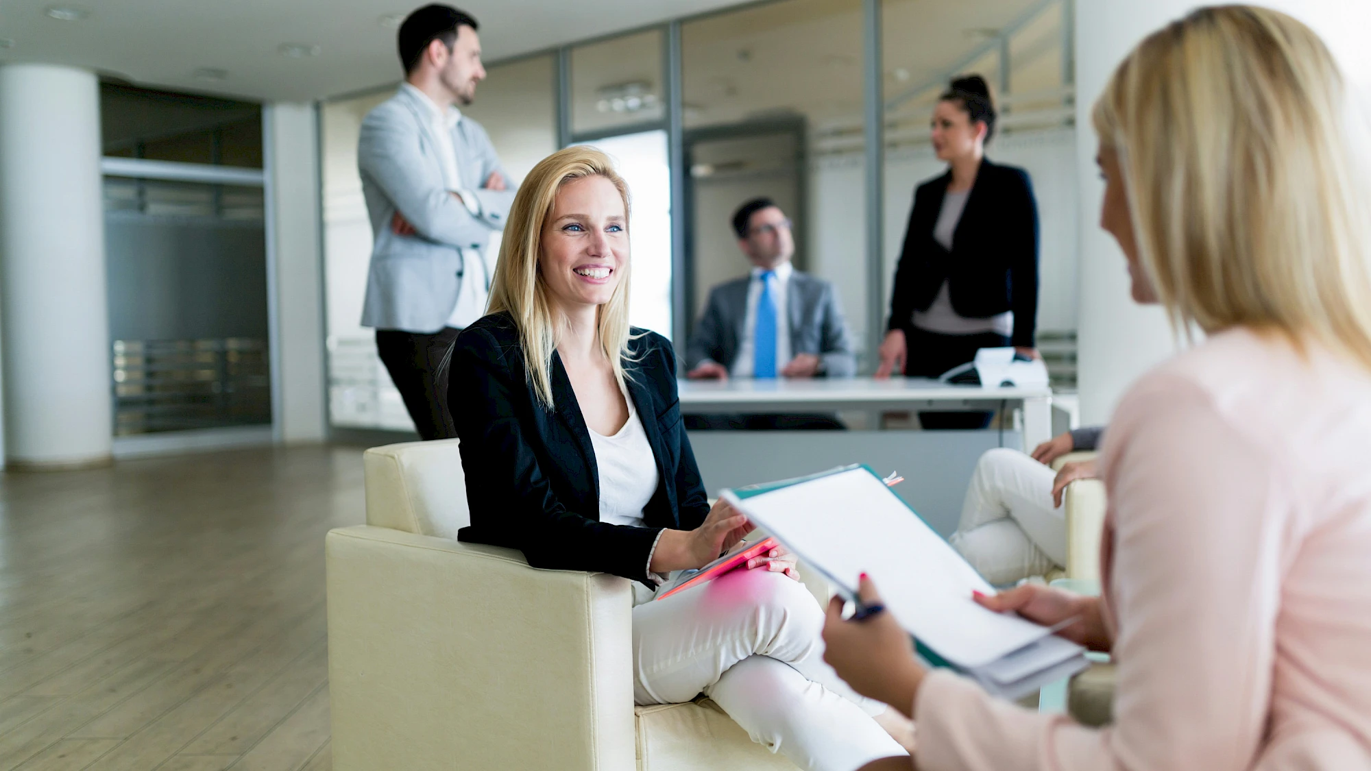 Két nő egyeztet a többi munkatárs jelenlétében