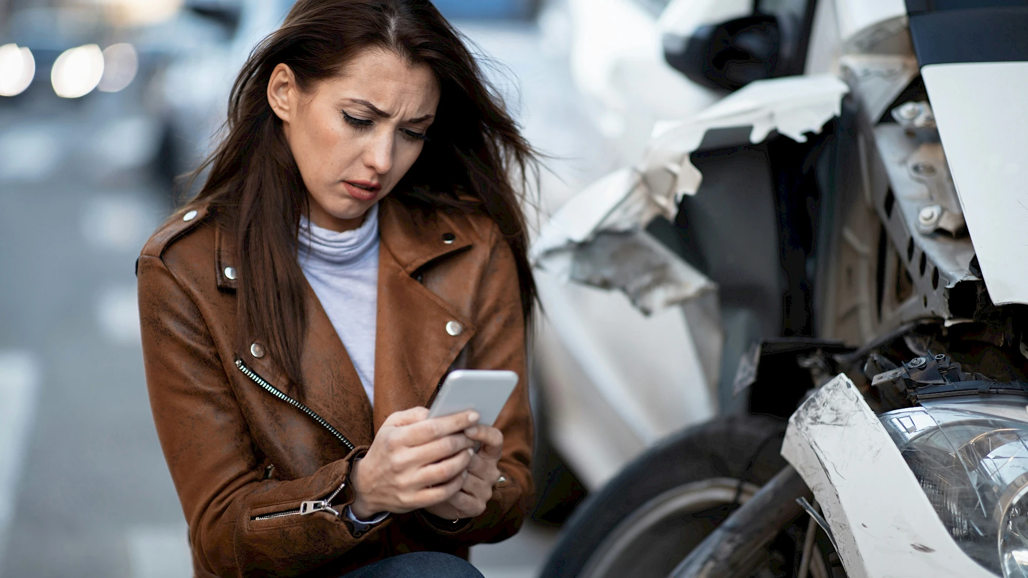 Nő a törött autó mellett nézi a telefonját